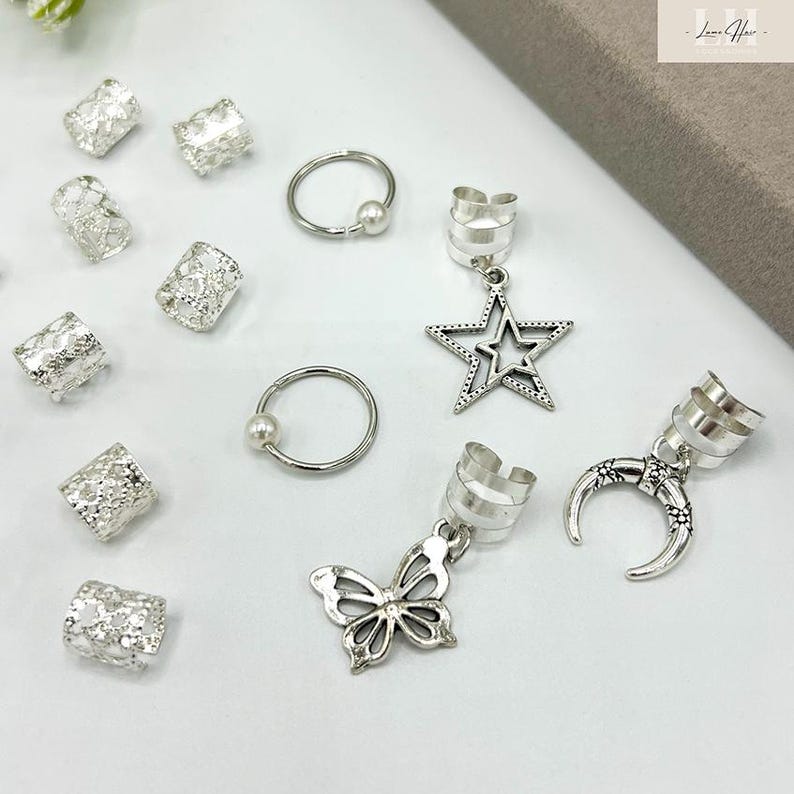 May include: An assortment of silver-colored hair accessories, including hair cuffs, rings, and decorative charms. Charms include a star, butterfly, and crescent moon. The hair cuffs are designed to be placed on the hair. The rings have a small pearl.