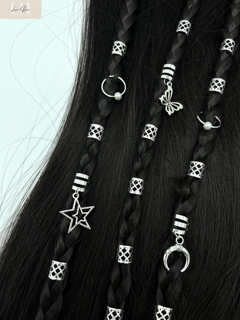 May include: Close-up of black braided hair adorned with silver hair beads and charms. Charms include a butterfly, star, crescent moon, and small rings. The beads have a geometric design. The hair accessories add a decorative touch to the hairstyle.