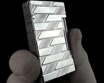 May include: A rectangular silver-toned metal lighter featuring a polished finish with a repeating geometric pattern of diagonal lines and smooth, raised rectangular segments across the front surface and the side panel of the lighter body.