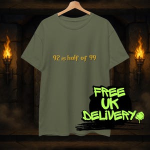 Puede incluir: Camiseta verde oliva con el texto "92 is half of 99" en letras doradas. La camiseta está colgada de una percha de madera. Un gráfico negro y verde que dice "FREE UK DELIVERY" está en la parte inferior derecha.