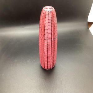 Puede incluir: Un jarrón alto y cilíndrico en un tono rojo intenso. El jarrón tiene una superficie texturizada con un patrón rectangular repetido. La parte superior del jarrón tiene un diseño ligeramente acampanado y acanalado. El jarrón está de pie.