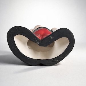 May include: A ceramic figurine with a black base and a red interior. The figurine has a heart-shaped design with a white interior and a black border. The figurine is set against a white background.
