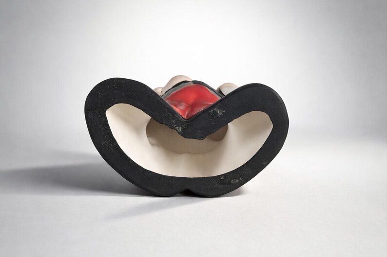 May include: A ceramic figurine with a black base and a red interior. The figurine has a heart-shaped design with a white interior and a black border. The figurine is set against a white background.
