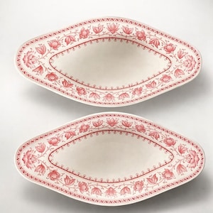 May include: Two oval-shaped serving platters with a cream-colored center and a red floral border. The floral design includes leaves and flowers. The platters are displayed on a white background.