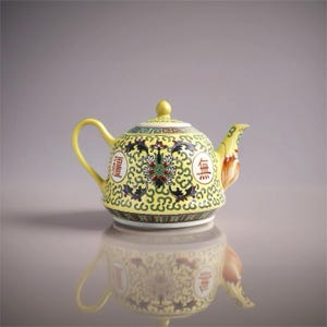 May include: A yellow ceramic teapot with a curved handle and spout. The teapot features a floral and scroll design in black, red, and green on a yellow background. The teapot has Chinese characters on the side.