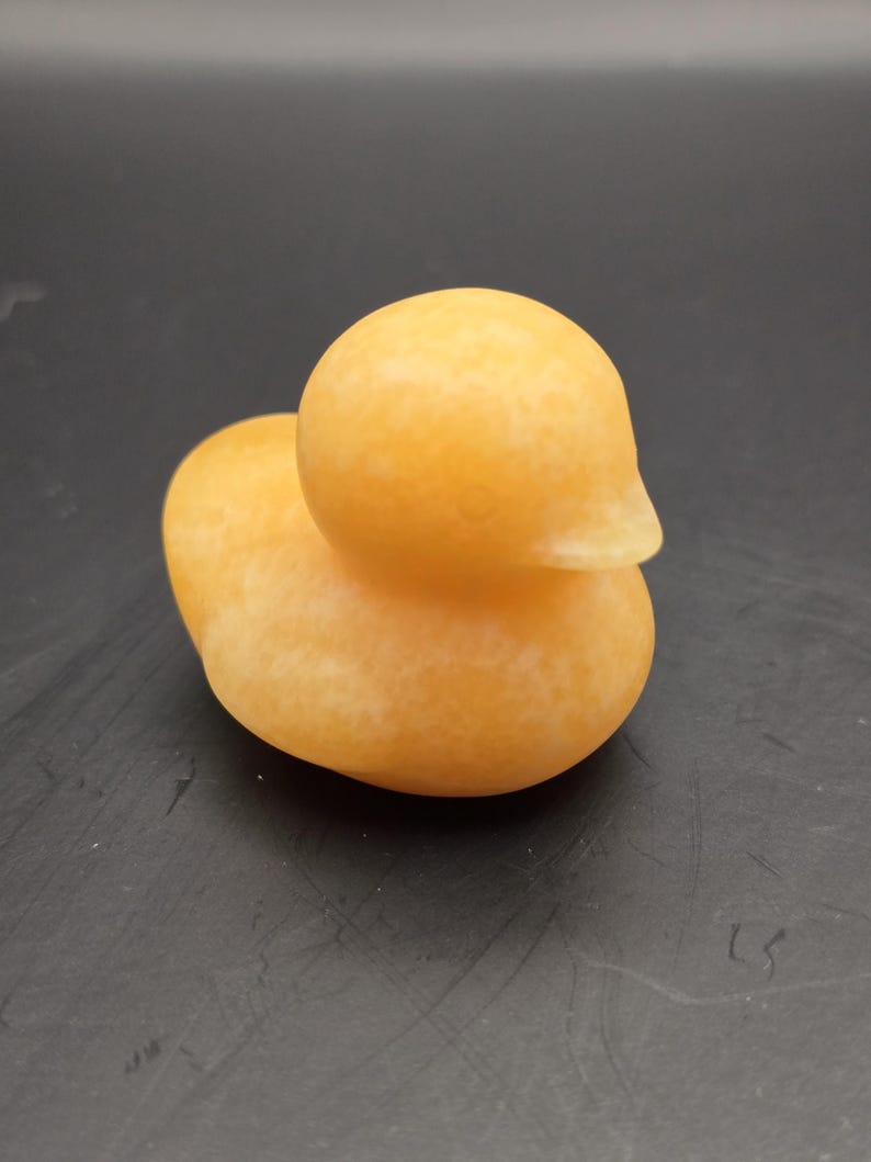 May include: A small, orange-yellow duck figurine. The duck has a smooth, rounded body and a small, pointed beak. The figurine is made of a solid material and has a slightly textured surface. The duck is a decorative item.