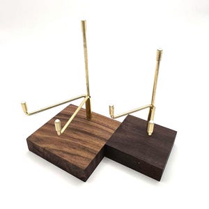 Op de afbeelding: Twee displaystandaards met vierkante houten voetstukken in verschillende bruintinten, elk voorzien van een verticale steunstructuur van messing. De messing armen steken naar buiten en hebben kleine cilindrische dopjes aan de uiteinden.