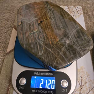 Puede incluir: Una piedra de labradorita pulida con vetas iridiscentes grises, marrones y doradas sobre una b&aacute;scula de cocina digital plateada y azul. La pantalla muestra un peso de 2120 gramos, con una capacidad m&aacute;xima de 10000g y una graduaci&oacute;n de 1g.
