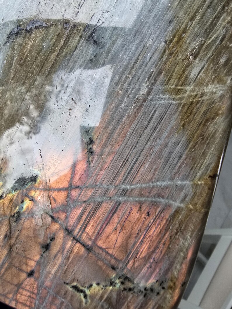 Puede incluir: Una losa pulida de piedra labradorita con una superficie lisa y reflectante con inclusiones naturales. El mineral muestra un espectro de colores iridiscentes, incluyendo tonos cobre profundo, bronce y gris apagado con estr&iacute;as lineales visibles.