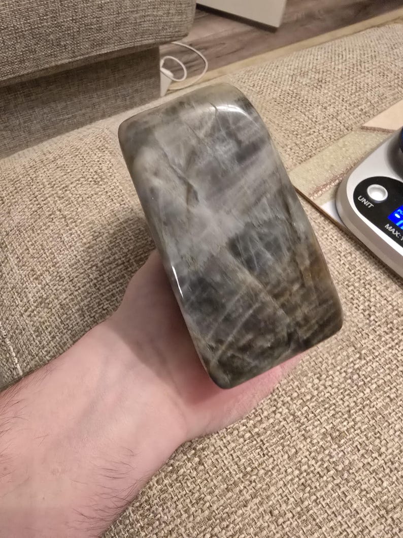 Puede incluir: Un bloque rectangular pulido de piedra gris y marr&oacute;n con vetas internas visibles y una superficie lisa y reflectante. La piedra presenta un aspecto jaspeado con varios tonos de carb&oacute;n, topo y blanco, mostrando una textura cristalina natural en toda la pieza.