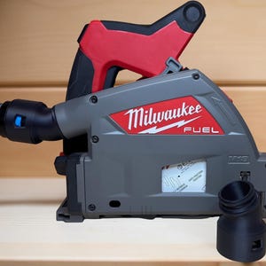 Peut inclure: Un outil électrique Milwaukee FUEL gris et rouge avec une poignée noire et un tuyau flexible attaché. L'outil porte le logo Milwaukee et une buse noire est détachée et placée devant l'outil.