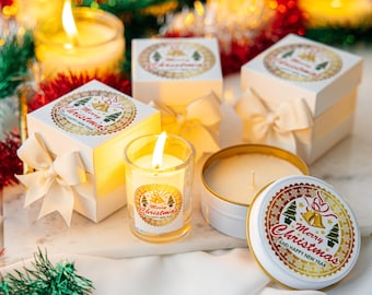 Könnte beinhalten: Eine festliche Weihnachtsdekoration mit brennenden Kerzen in Glas- und Metalldosen sowie Geschenkboxen mit cremefarbenen Schleifen. Die Boxen und Kerzendeckel sind mit einem gold-roten "Merry Christmas" Design verziert. Dekorative Girlanden verstärken die festliche Atmosphäre.