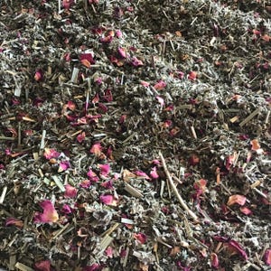 Puede incluir: Primer plano de una mezcla de hierbas secas y p&eacute;talos de rosa. La mezcla presenta varias hierbas y tallos verdes, con trozos dispersos de p&eacute;talos de rosa rosados. La textura es densa y natural, lo que sugiere una infusi&oacute;n de hierbas o popurr&iacute;.