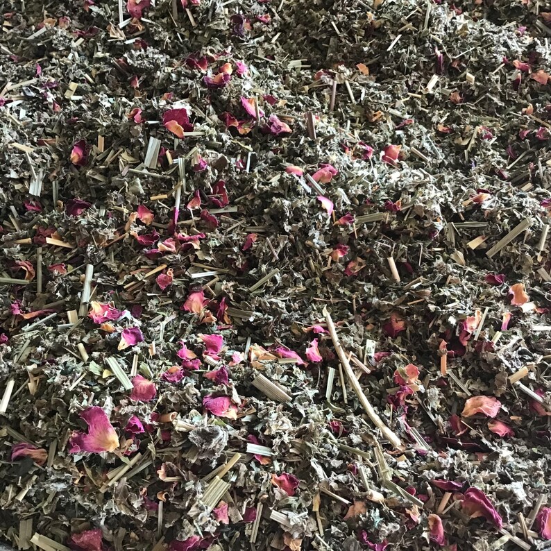 Puede incluir: Primer plano de una mezcla de hierbas secas y p&eacute;talos de rosa. La mezcla presenta varias hierbas y tallos verdes, con trozos dispersos de p&eacute;talos de rosa rosados. La textura es densa y natural, lo que sugiere una infusi&oacute;n de hierbas o popurr&iacute;.