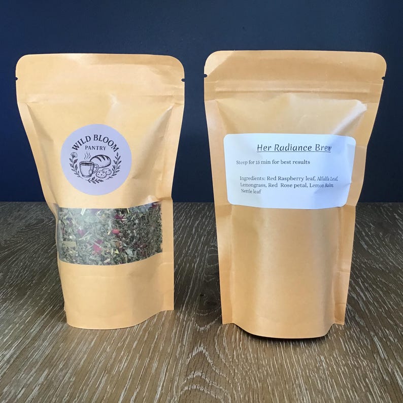 Puede incluir: Dos bolsas de t&eacute; color beige. Una muestra la mezcla de t&eacute; a trav&eacute;s de una ventana transparente. La otra tiene una etiqueta que dice "Her Radiance Brew". Los ingredientes incluyen hoja de frambuesa roja, hoja de alfalfa, hierba de lim&oacute;n, p&eacute;talo de rosa roja, melisa y hoja de ortiga.