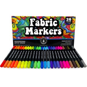 May include: A set of 26 fabric markers with dual tips, displayed in front of a box with the words "Fabric Markers" and a colorful psychedelic design. The markers are in various vibrant colors, perfect for fabric art projects.