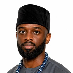 Puede incluir: Retrato de un hombre con una gorra de terciopelo negro y una camisa gris. Tiene barba completa y un collar de cuentas con cuentas azules y blancas. El fondo es blanco liso.