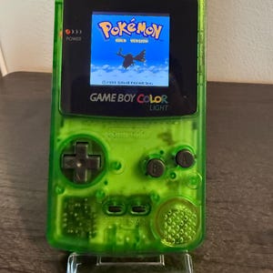 Puede incluir: Una taza de cerámica blanca con un asa negra y el texto "But First, Coffee" en negro y negrita. La taza está sobre una superficie de madera. La taza mide aproximadamente 10 cm de alto.