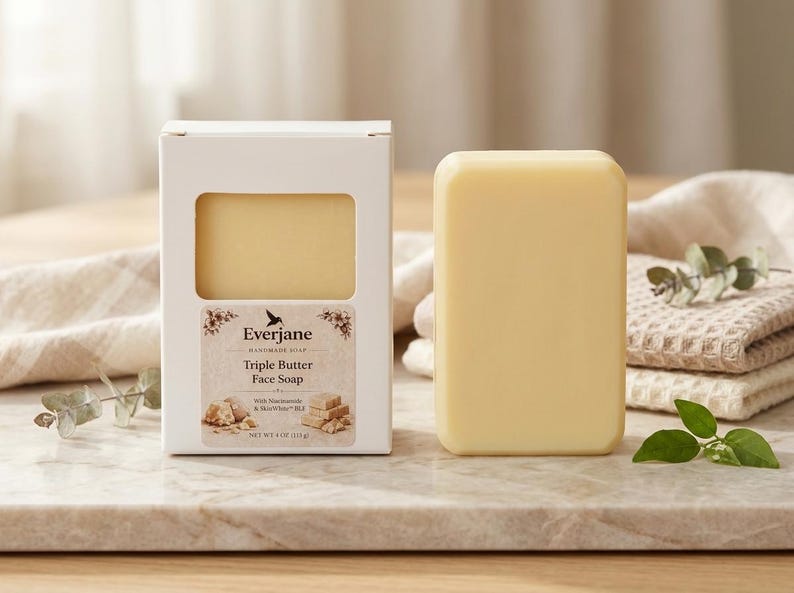 May include: A light yellow Triple Butter Face Soap bar next to its white box. The box has a window showing the soap and a label with the brand name and product details. The soap is 113g.