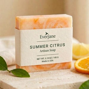 Puede incluir: Una pastilla de jab&oacute;n rectangular con vetas naranjas y blancas, envuelta en una etiqueta de papel color crema. La etiqueta muestra el texto Everjane, SUMMER CITRUS, Artisan Soap y NET WT. 5.10 OZ | 145 G, Made in USA en letras negras.