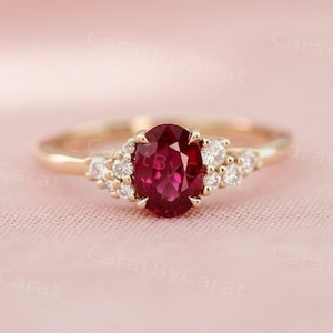 以下が含まれることがあります： 中央に楕円形のルビーを配したゴールドリング。ルビーは深い赤色で、周囲には小さなクリアな宝石が散りばめられています。リングのバンドは繊細なゴールドカラーで、全体的にエレガントでクラシックなデザインです。