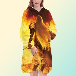 May include: A hooded blanket featuring a warrior figure with long, flowing hair, set against a fiery, yellow and red background. The design is printed on a soft, oversized blanket, perfect for cozy comfort.