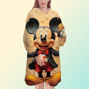 K&ouml;nnte beinhalten: Eine Kapuzen-Decke mit einer farbenfrohen Illustration von Mickey Mouse im Smoking. Die Decke ist &uuml;berwiegend gelb und hat eine weiche, flauschige Textur. Mickey tr&auml;gt eine rote Fliege, rote Shorts und gelbe Schuhe.