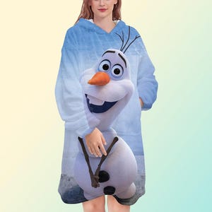 May include: A blue hooded blanket featuring a smiling Olaf from Frozen. The blanket has a light blue background with a snowy design and a large Olaf graphic on the front. It has long sleeves and a front pocket.