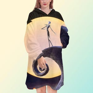 Puede incluir: Una manta con capucha con un dise&ntilde;o de Pesadilla antes de Navidad. El dise&ntilde;o muestra a Jack Skellington de pie en una colina con una luna llena de fondo. La manta es negra con el interior blanco.