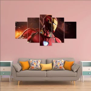 Puede incluir: Un conjunto de arte mural en lienzo de cinco paneles que presenta a Iron Man en una pose din&aacute;mica. La obra de arte muestra al personaje con su ic&oacute;nica armadura roja y dorada, sobre un fondo ardiente. Los paneles est&aacute;n dispuestos encima de un sof&aacute; gris con cojines coloridos.