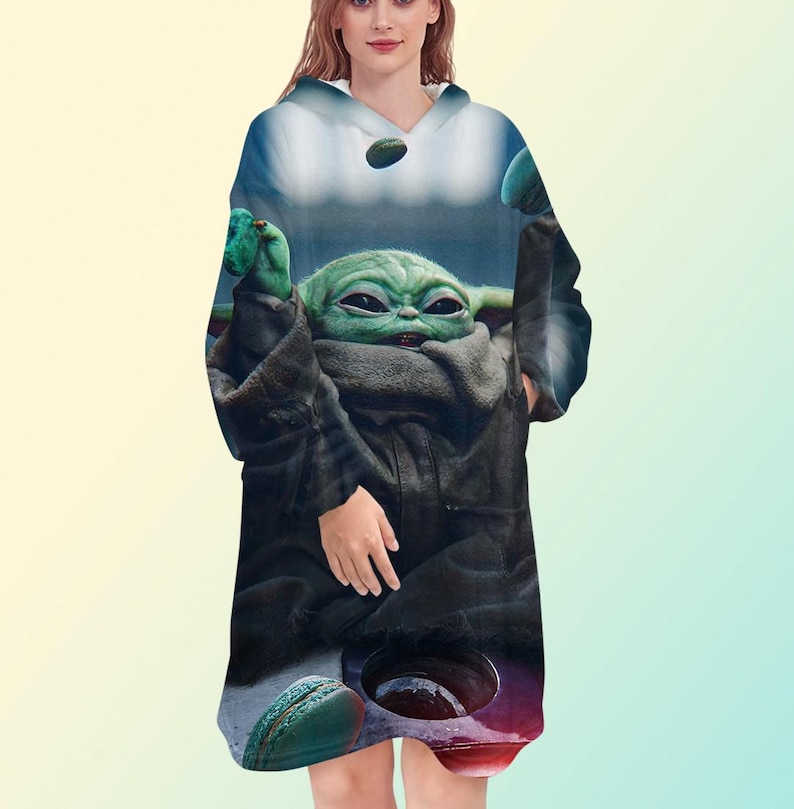 May include: A hooded sweatshirt featuring a graphic of a green alien character with large eyes and ears. The design includes a dark cloak and a background with blue and green tones. The sweatshirt has a v-neck and a relaxed fit.