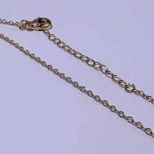 May include: A gold-colored necklace chain with a lobster clasp and an extender chain. The chain is composed of small, oval-shaped links. The clasp and extender chain are also gold-colored.