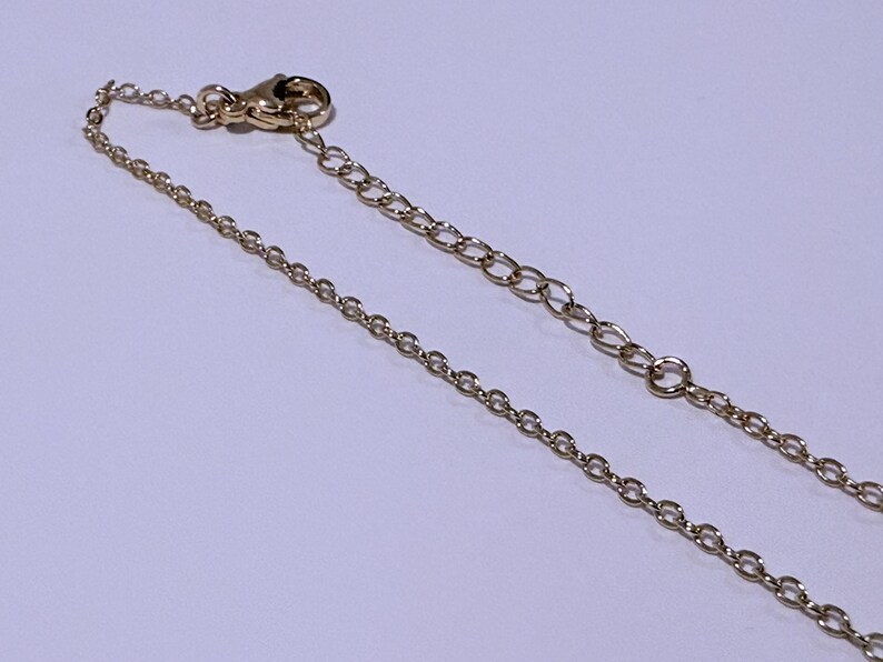 May include: A gold-colored necklace chain with a lobster clasp and an extender chain. The chain is composed of small, oval-shaped links. The clasp and extender chain are also gold-colored.