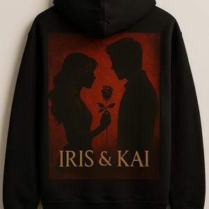 Puede incluir: Sudadera con capucha negra con una silueta de pareja, con una mujer sosteniendo una rosa. El fondo es rojo y el texto "IRIS & KAI" es dorado. Diseño romántico.