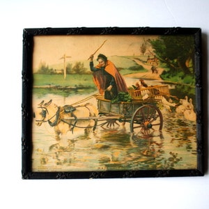 May include: Framed vintage print depicting a person in a cart pulled by two donkeys crossing a body of water. The cart carries produce and fowl. The print is in a black ornate frame.