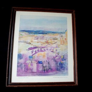 May include: A framed watercolor painting of a city landscape with a bridge in the distance. The painting is in shades of purple, blue, and yellow. The artist's signature is in the bottom right corner.