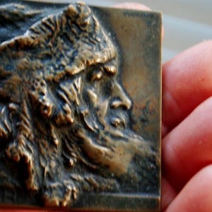 Peut inclure: Une sculpture en bronze en relief représentant une personne portant un chapeau de fourrure et une barbe. La sculpture est détaillée et texturée, avec une représentation réaliste des traits du visage de la personne.