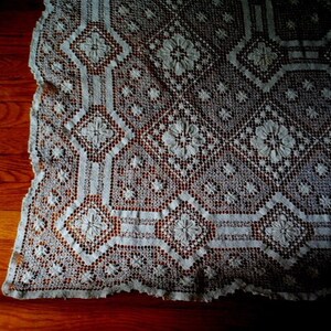 K&ouml;nnte beinhalten: Eine wei&szlig;e H&auml;keltischdecke mit einem zarten Blumenmuster. Die Tischdecke ist aus feiner Spitze und hat einen gewellten Rand.