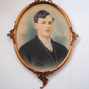 May include: A vintage oval portrait of a young man in a dark suit and white shirt, framed in a gold ornate frame.