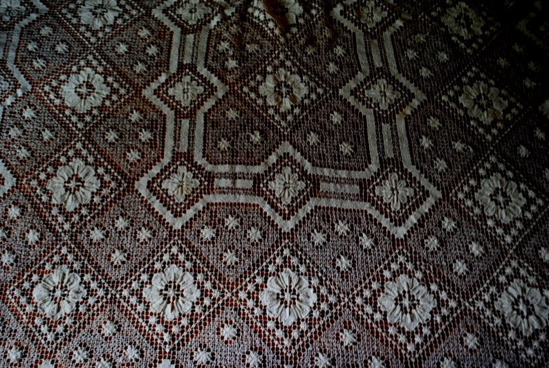 K&ouml;nnte beinhalten: Nahaufnahme einer wei&szlig;en H&auml;keltischdecke mit einem zarten Blumenmuster. Die Tischdecke hat einen dunkelbraunen Hintergrund, der einen Kontrast zwischen den hellen und dunklen Farben erzeugt.