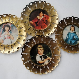 May include: Four gold-toned metal frames with ornate butterfly designs. Each frame holds a vintage portrait of a child. The portraits feature a girl in a white dress, a boy in a red suit, a girl in a blue dress, and a girl with a dog.