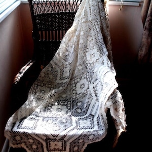 K&ouml;nnte beinhalten: Eine wei&szlig;e H&auml;keltischdecke, die &uuml;ber einen Korbstuhl gelegt ist. Die Spitze hat ein zartes Blumenmuster und ist ein wundersch&ouml;nes Beispiel f&uuml;r Vintage-Handwerk.