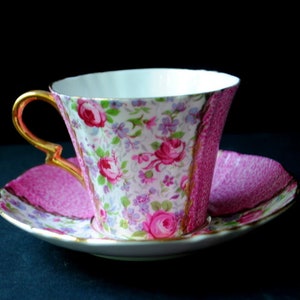 May include: A pink and white teacup and saucer set with a floral pattern. The cup has a gold trim and a delicate handle. The saucer has a pink rim and a floral pattern.