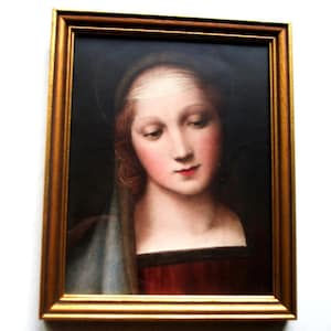 Puede incluir: Una pintura enmarcada de una mujer con cabello largo y castaño que lleva una cubierta blanca para la cabeza y un vestido rojo. La pintura está sobre un fondo oscuro.