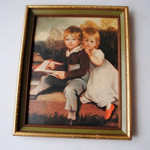 May include: Framed painting of two children, a boy and a girl, sitting on a stone wall. The boy is drawing in a book while the girl looks on. The painting is set in a lush green landscape.