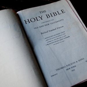 Könnte beinhalten: Eine Nahaufnahme eines weißen Buches mit dem Titel "The Holy Bible" auf dem Einband. Das Buch enthält das Alte und das Neue Testament und ist die revidierte Standardversion. Das Buch wurde 1953 von Thomas Nelson & Sons herausgegeben.