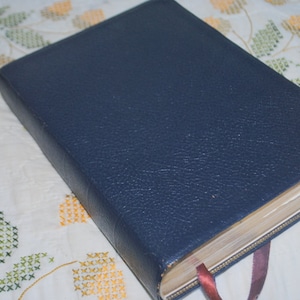 Könnte beinhalten: Ein dunkelblaues, ledergebundenes Buch mit einem abgenutzten, strukturierten Einband und einem Lesezeichen aus Band.