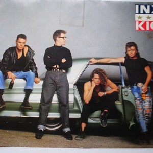 May include: A promotional poster featuring the band INXS. The band members are posed in front of a vintage car. The poster has the band's name and album title "KICK" in a red, white, and blue design.