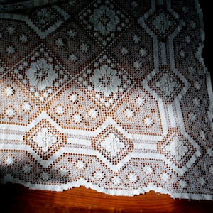 K&ouml;nnte beinhalten: Wei&szlig;e Spitzentischdecke mit einem zarten Blumenmuster. Die Spitze ist filigran und hat einen Vintage-Look.