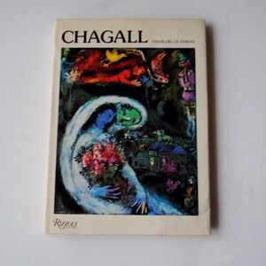 May include: A book titled "Chagall" by Francois Le Targat, featuring a colorful painting on the cover depicting a couple with a bouquet of flowers, a village scene, and a flying figure with a bird.